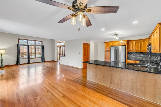 kitchen featuring light hardwood / wood-style flooring, kitchen peninsula, dark stone counters, decorative backsplash, and appliances with stainless steel finishes