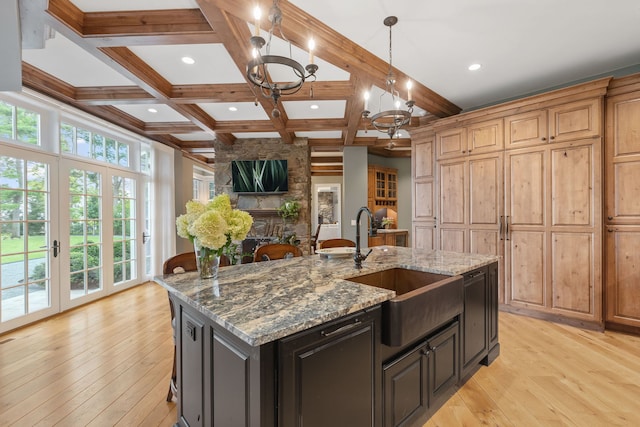 kitchen featuring coffered ceiling, light stone countertops, a large island with sink, beam ceiling, and sink