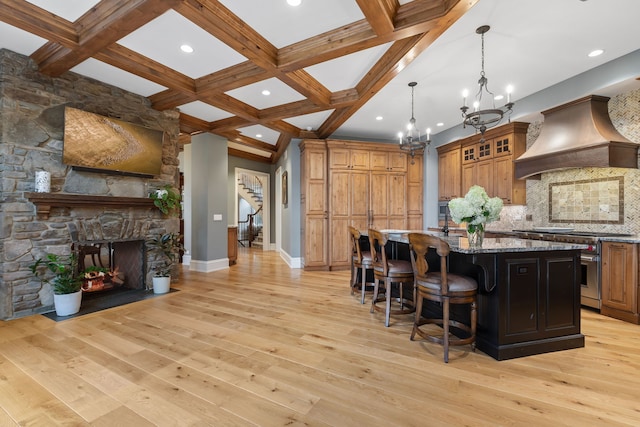 kitchen with custom exhaust hood, coffered ceiling, a spacious island, light stone countertops, and light hardwood / wood-style flooring