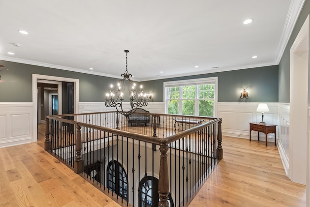 corridor with light hardwood / wood-style floors, crown molding, and a notable chandelier