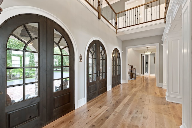 foyer entrance featuring french doors, a towering ceiling, ornamental molding, and light hardwood / wood-style floors