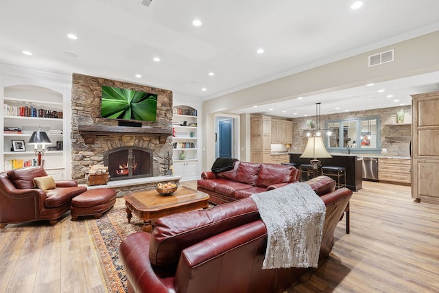 living room featuring light hardwood / wood-style floors, built in features, crown molding, and a stone fireplace