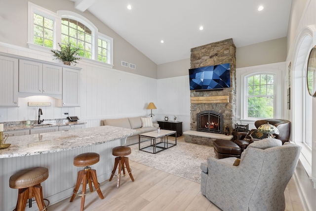 living room featuring light hardwood / wood-style floors, sink, high vaulted ceiling, and a fireplace