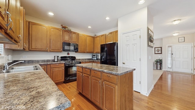 kitchen with sink, a kitchen island, black appliances, and light wood-type flooring