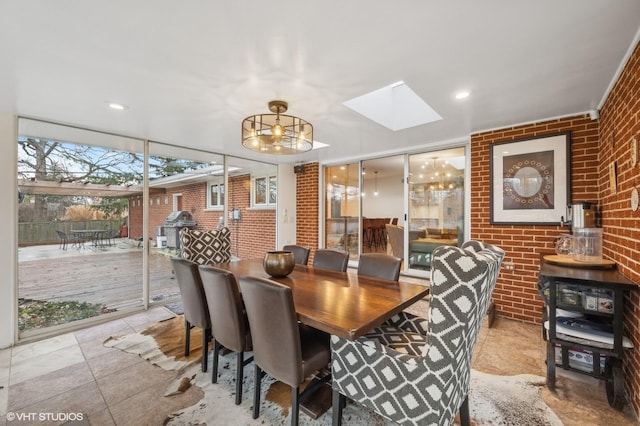 dining area with a chandelier, a skylight, floor to ceiling windows, and brick wall