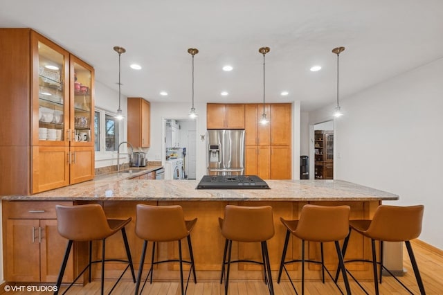 kitchen with kitchen peninsula, appliances with stainless steel finishes, light stone counters, sink, and light hardwood / wood-style flooring