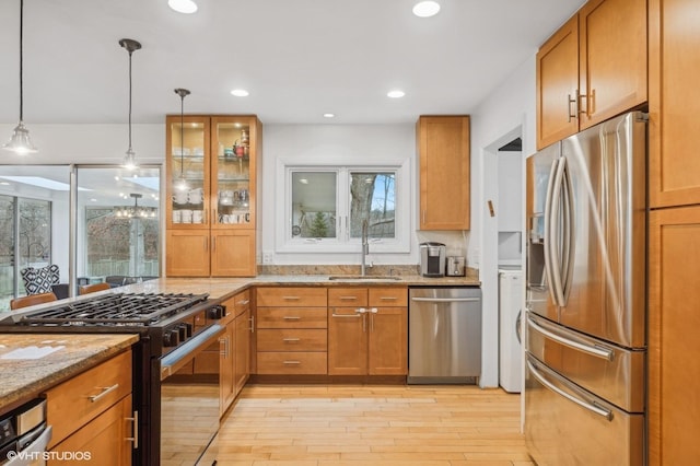 kitchen with sink, stainless steel appliances, light stone counters, light hardwood / wood-style flooring, and decorative light fixtures