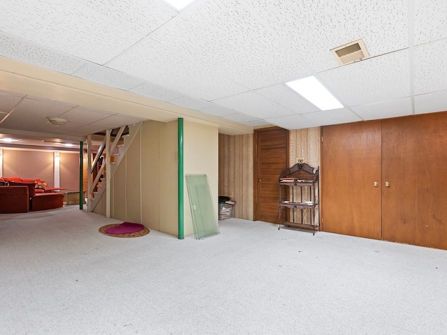 basement with carpet flooring, a paneled ceiling, and wood walls