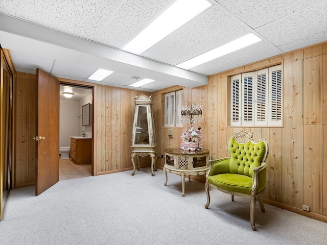 living area featuring a drop ceiling, light carpet, and wooden walls