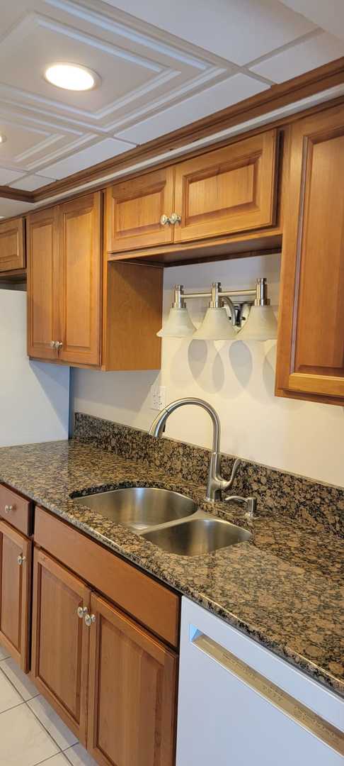 kitchen with white dishwasher, dark stone countertops, light tile patterned floors, and sink