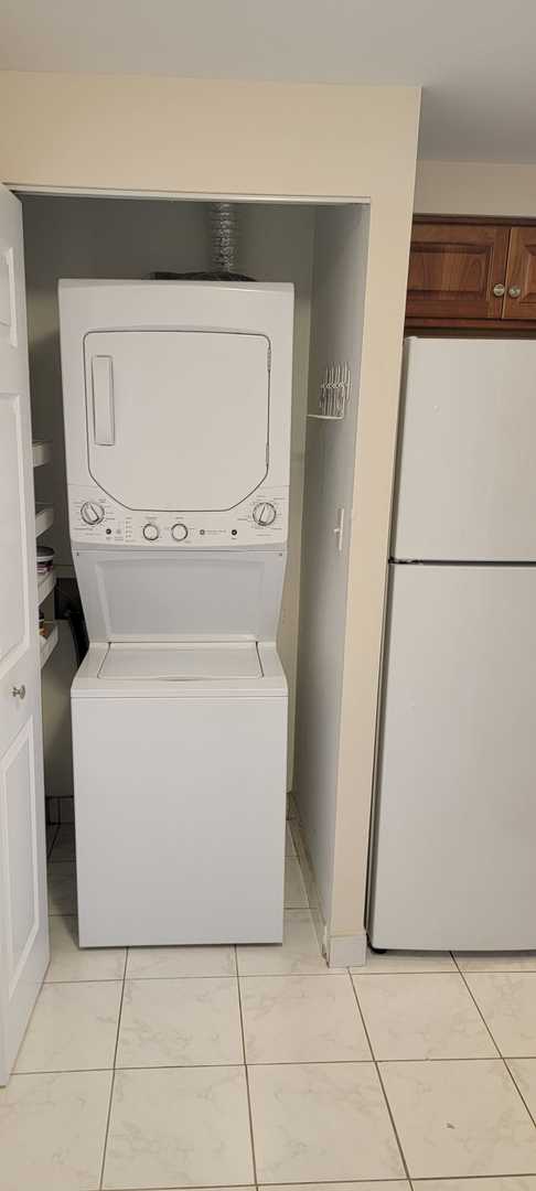 laundry area with stacked washer / drying machine and light tile patterned floors