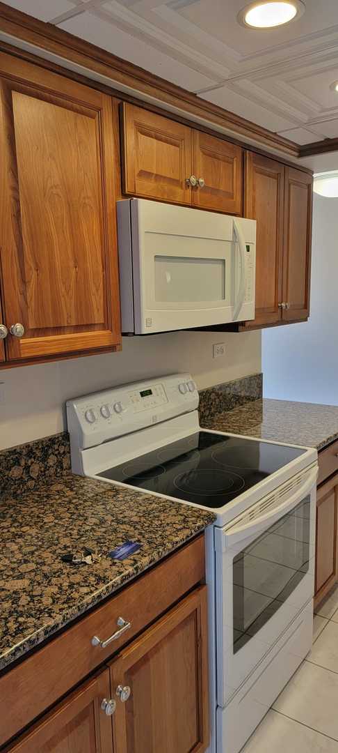 kitchen featuring light tile patterned flooring, white appliances, and dark stone counters