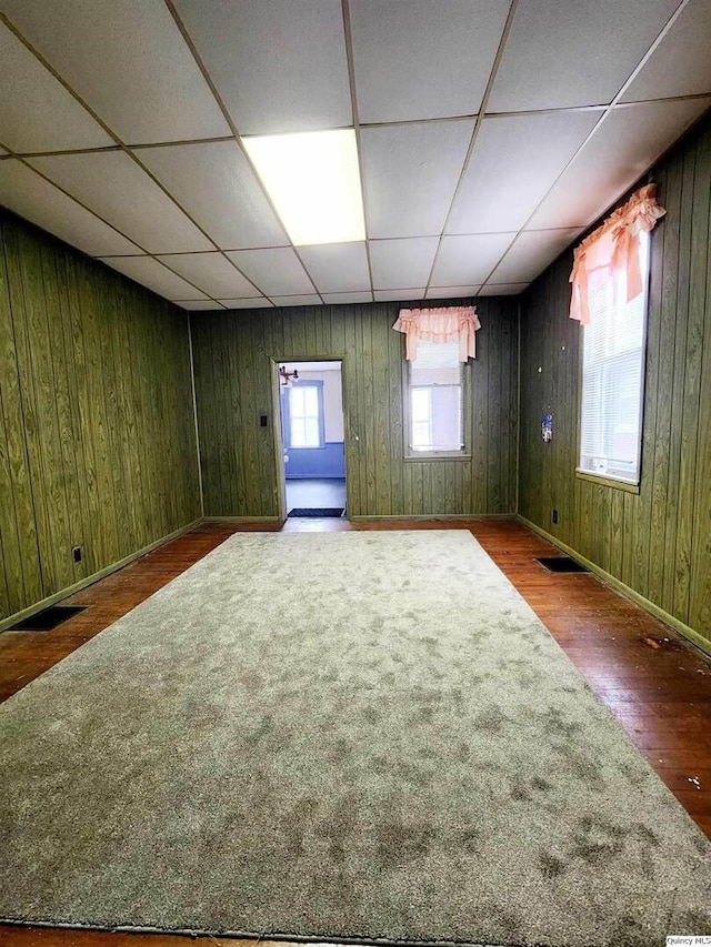 basement featuring wood-type flooring, a paneled ceiling, and wood walls