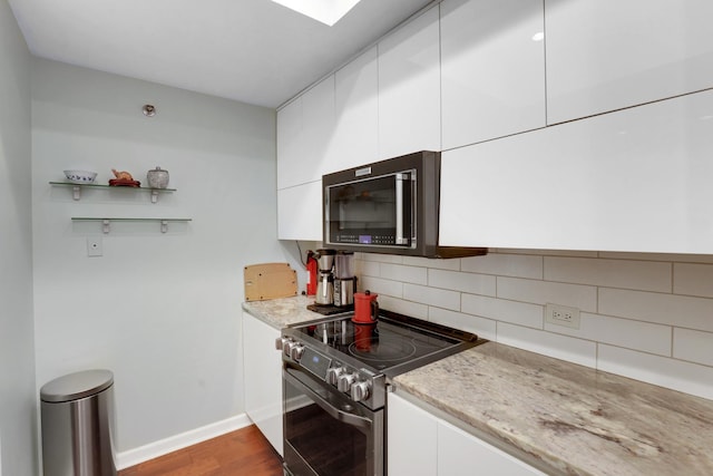 kitchen with decorative backsplash, light stone countertops, electric range, light hardwood / wood-style flooring, and white cabinets