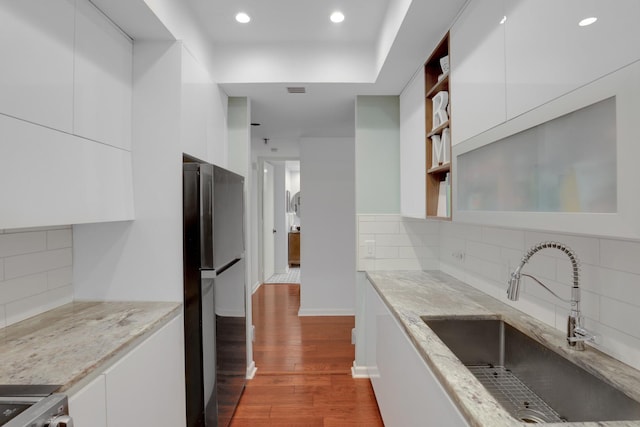 kitchen with stainless steel fridge, white cabinetry, sink, and light stone countertops