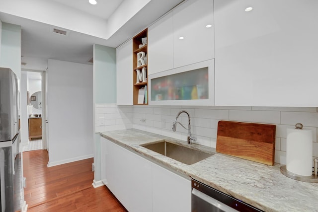 kitchen featuring backsplash, sink, light stone countertops, light hardwood / wood-style floors, and white cabinetry