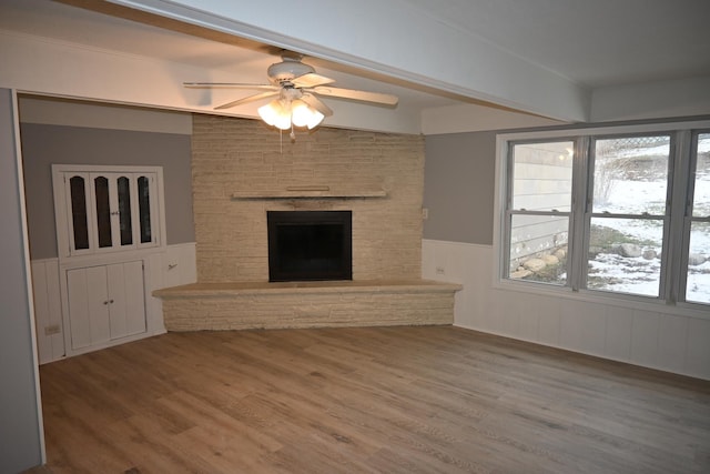 unfurnished living room with hardwood / wood-style floors, a stone fireplace, and ceiling fan