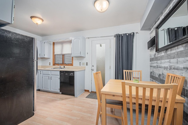 kitchen with wood walls, sink, black appliances, and light hardwood / wood-style flooring