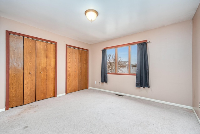 unfurnished bedroom with light colored carpet and multiple closets