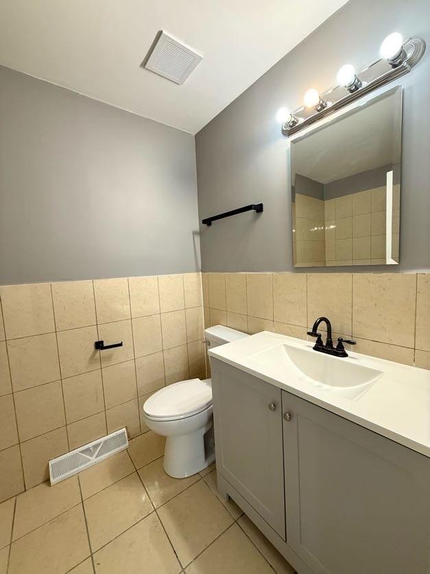 bathroom with toilet, vanity, tile patterned floors, and tile walls