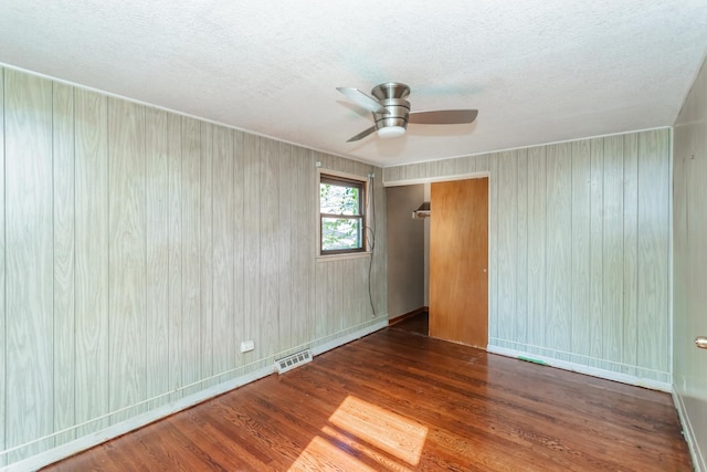 empty room featuring a textured ceiling, dark hardwood / wood-style floors, ceiling fan, and wooden walls