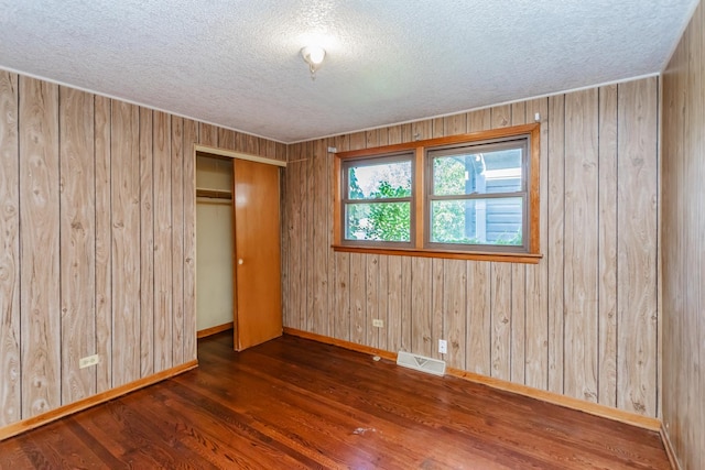 unfurnished bedroom with dark hardwood / wood-style flooring, wood walls, a closet, and a textured ceiling