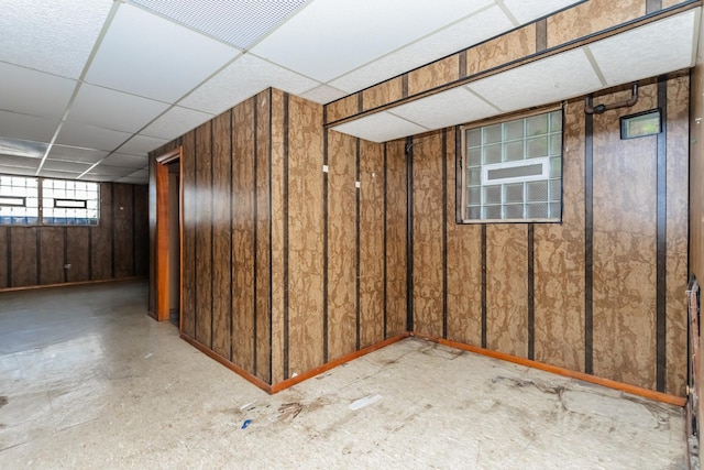 basement featuring a paneled ceiling and wooden walls