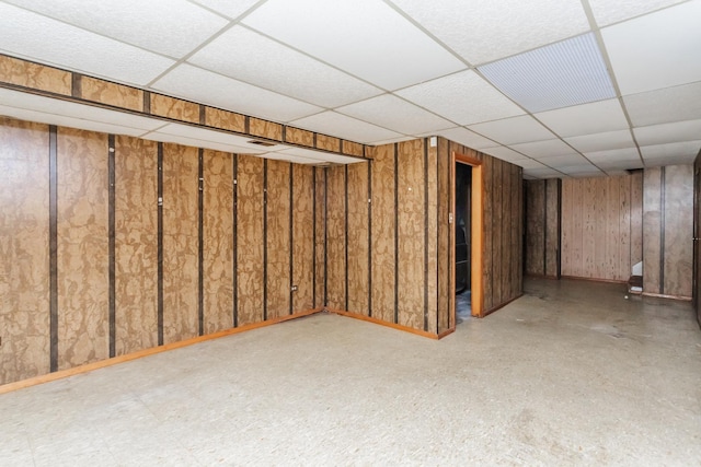 basement featuring a drop ceiling and wood walls