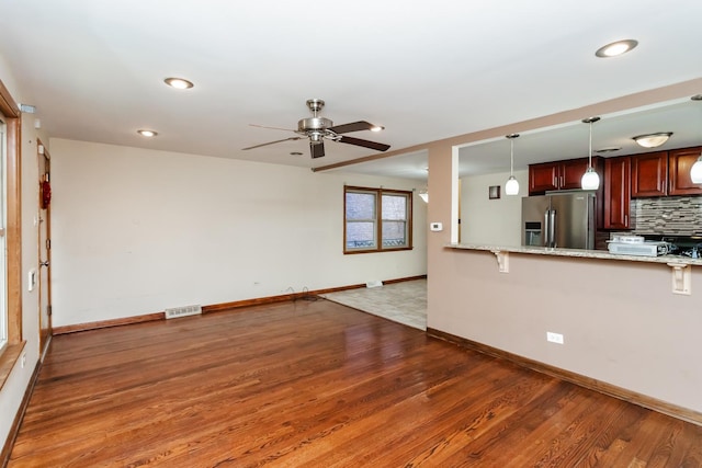 kitchen with kitchen peninsula, stainless steel refrigerator with ice dispenser, tasteful backsplash, light stone counters, and dark hardwood / wood-style floors