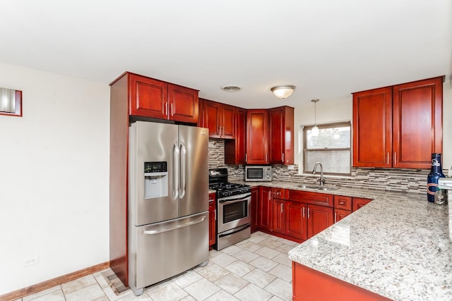 kitchen featuring appliances with stainless steel finishes, tasteful backsplash, light stone counters, sink, and hanging light fixtures