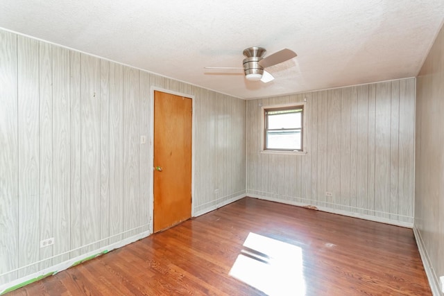 spare room featuring ceiling fan, wooden walls, wood-type flooring, and a textured ceiling