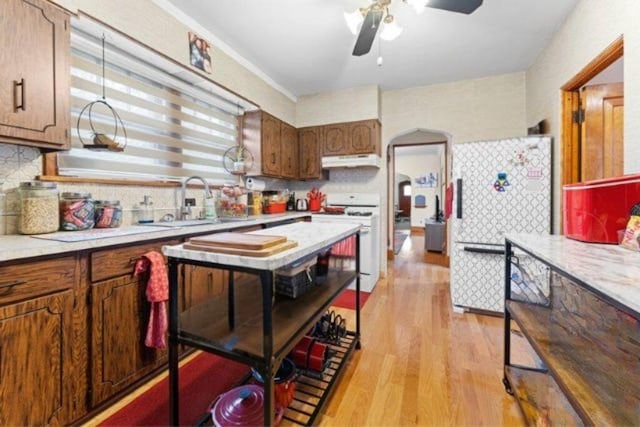 kitchen with white refrigerator, sink, light wood-type flooring, tasteful backsplash, and range