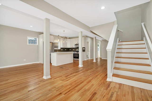 unfurnished living room featuring light wood-type flooring, sink, and a chandelier