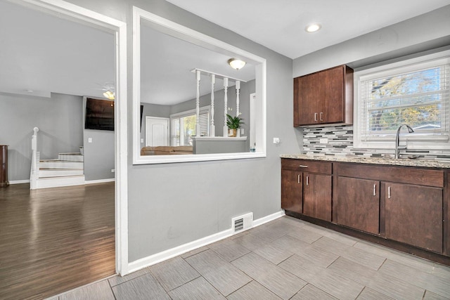 kitchen featuring light stone countertops, dark brown cabinets, and tasteful backsplash