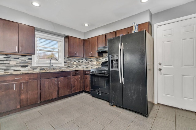 kitchen featuring light stone countertops, tasteful backsplash, dark brown cabinetry, sink, and black appliances