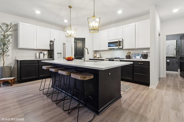 kitchen with sink, hanging light fixtures, an island with sink, high end white refrigerator, and light wood-type flooring