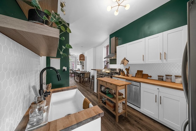 kitchen featuring wooden counters, wall chimney exhaust hood, appliances with stainless steel finishes, tasteful backsplash, and white cabinetry