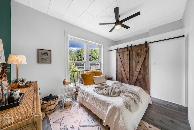 bedroom with wood-type flooring, a barn door, and ceiling fan