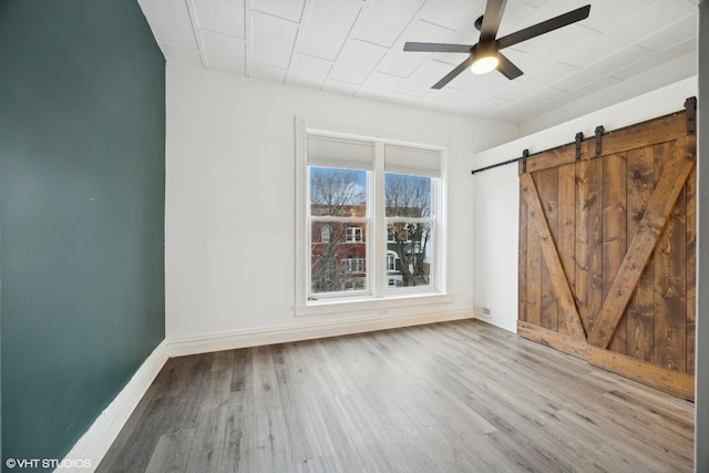 unfurnished room with hardwood / wood-style floors, a barn door, and ceiling fan