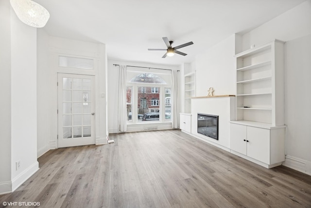 unfurnished living room with ceiling fan, light wood-type flooring, and built in shelves