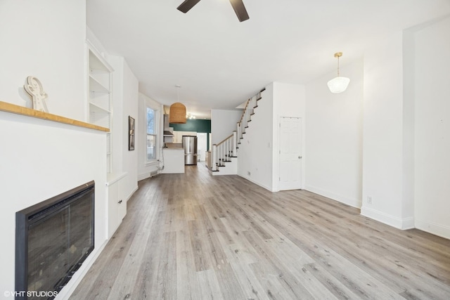 unfurnished living room featuring ceiling fan, light hardwood / wood-style floors, and built in shelves