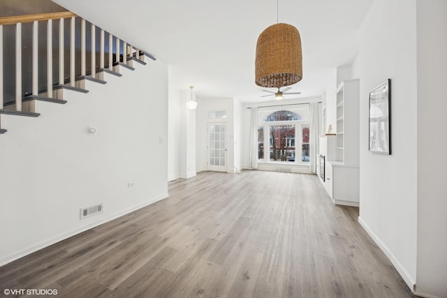 unfurnished living room with built in shelves, ceiling fan, and wood-type flooring