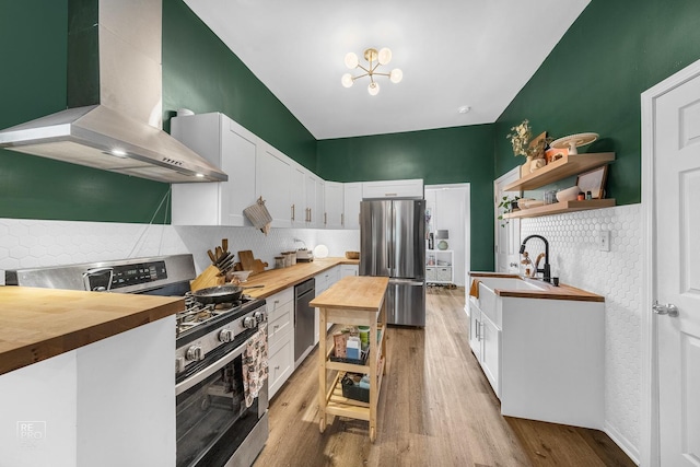 kitchen with butcher block countertops, wall chimney exhaust hood, white cabinets, and stainless steel appliances