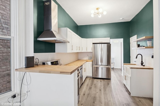 kitchen with wall chimney exhaust hood, light wood-type flooring, butcher block countertops, white cabinetry, and stainless steel refrigerator