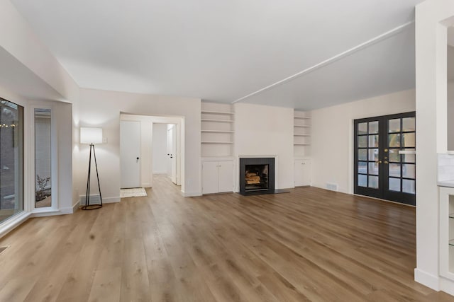 unfurnished living room featuring light hardwood / wood-style floors, built in features, and french doors