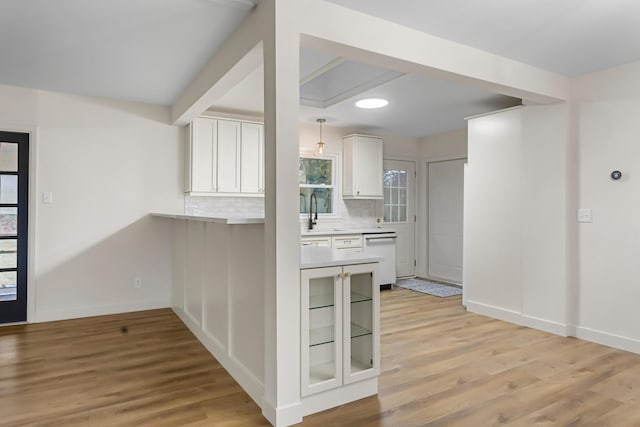 kitchen featuring backsplash, dishwasher, sink, white cabinetry, and light wood-type flooring