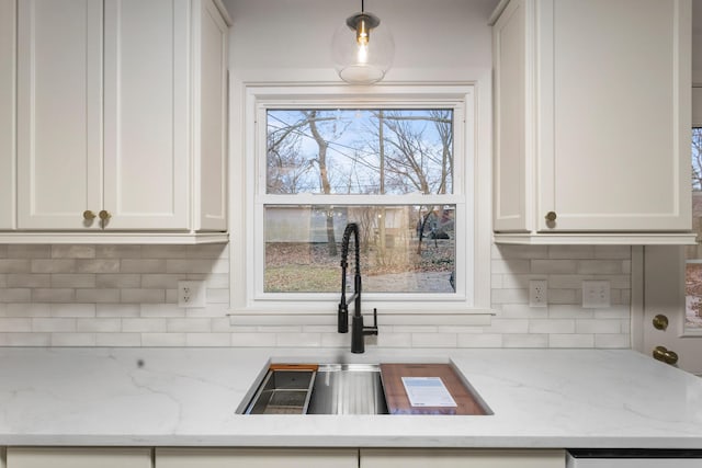 kitchen featuring decorative light fixtures, white cabinets, light stone countertops, and sink