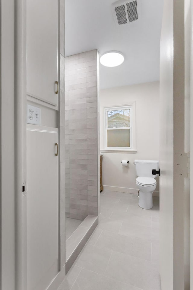 bathroom featuring toilet, tile patterned floors, and a tile shower