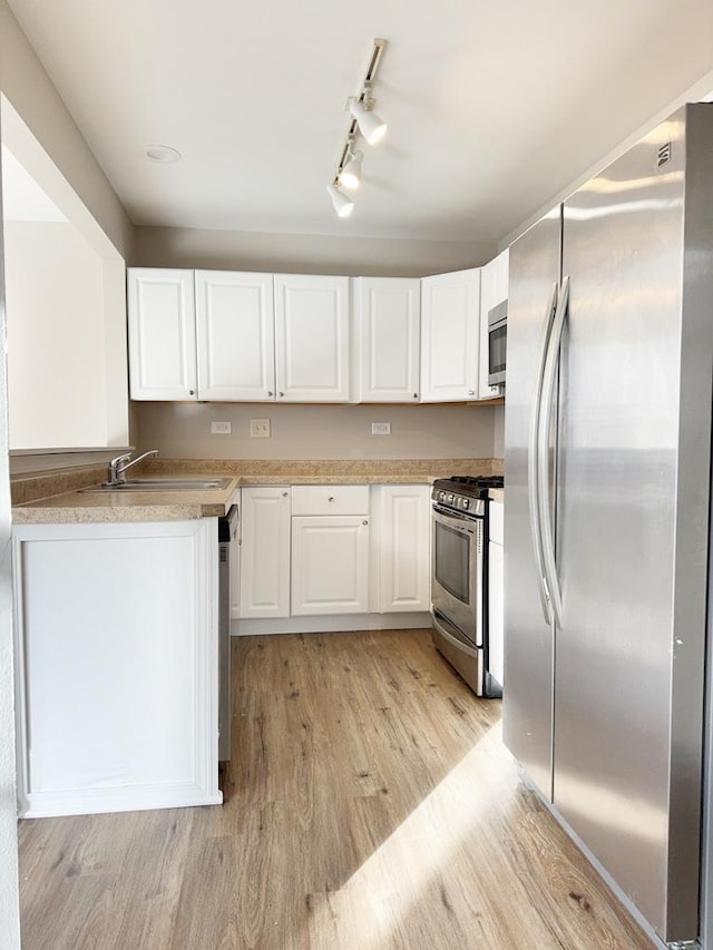 kitchen featuring light wood-type flooring, rail lighting, stainless steel appliances, sink, and white cabinetry