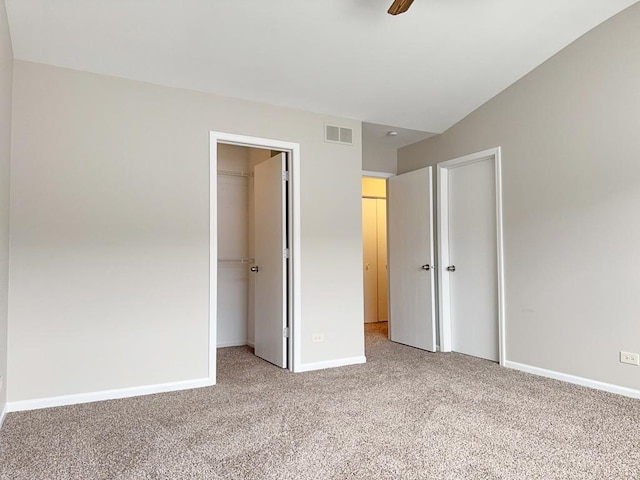 unfurnished bedroom with a walk in closet, ceiling fan, a closet, and carpet floors